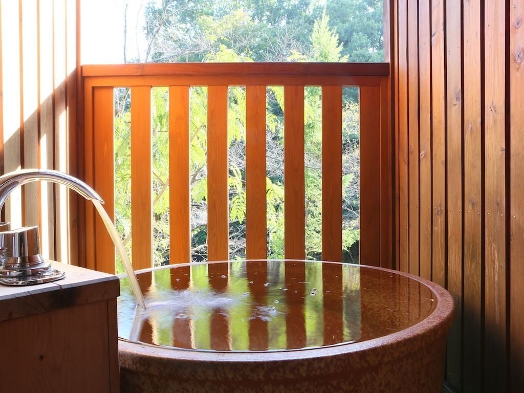 A wooden cabin with a circular stone sink and a window overlooking a forest.