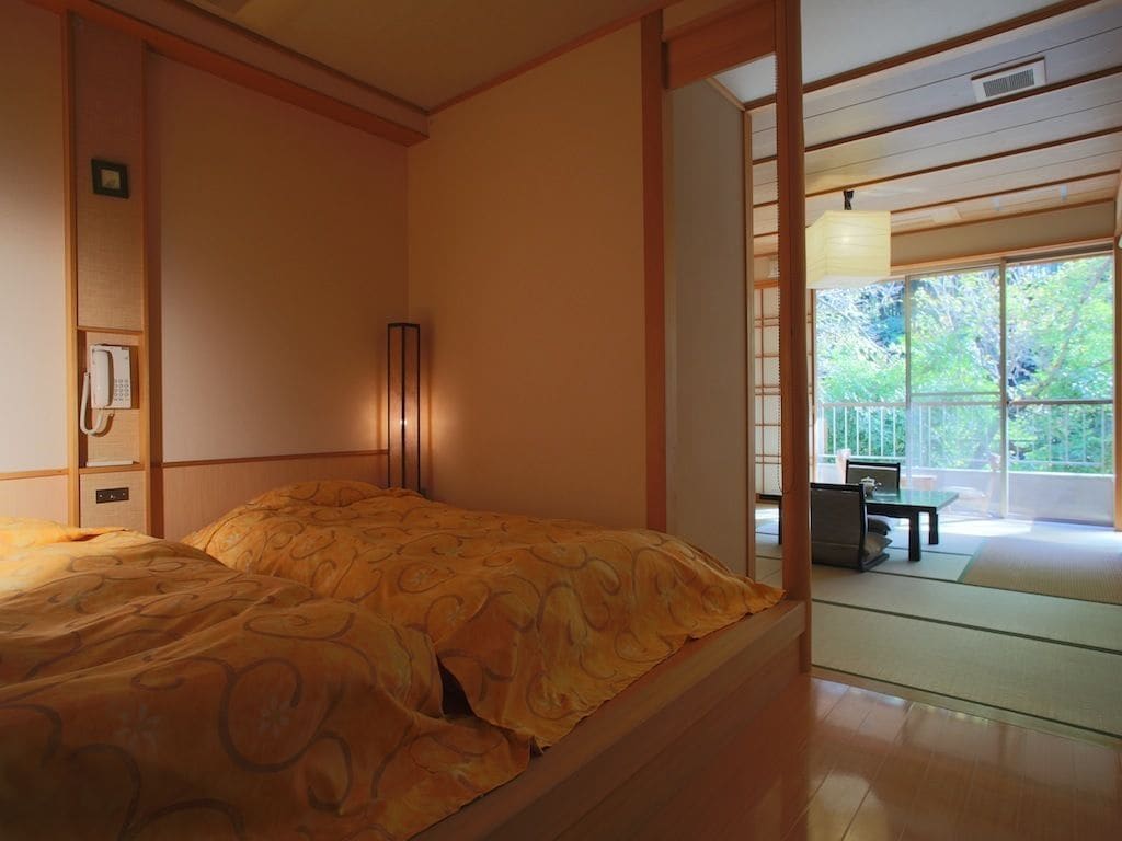 Une chambre de style japonais traditionnel, avec un lit, des portes coulissantes et une vue sur l’extérieur.