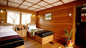 A wooden-paneled bedroom with two beds, a nightstand, a bedside table, a potted plant, and a framed picture on the wall. - Amara River Cruise (Mandalay)