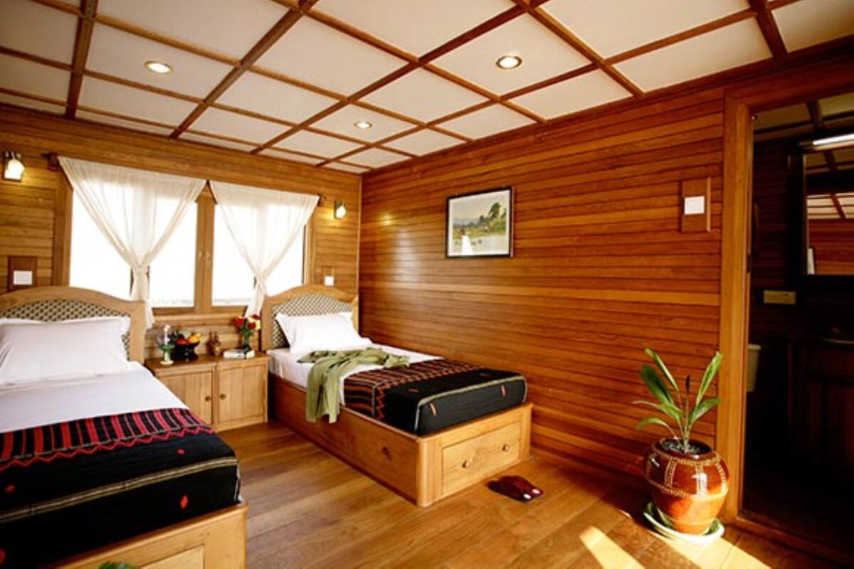 A wooden-paneled bedroom with two beds, a nightstand, a bedside table, a potted plant, and a framed picture on the wall.