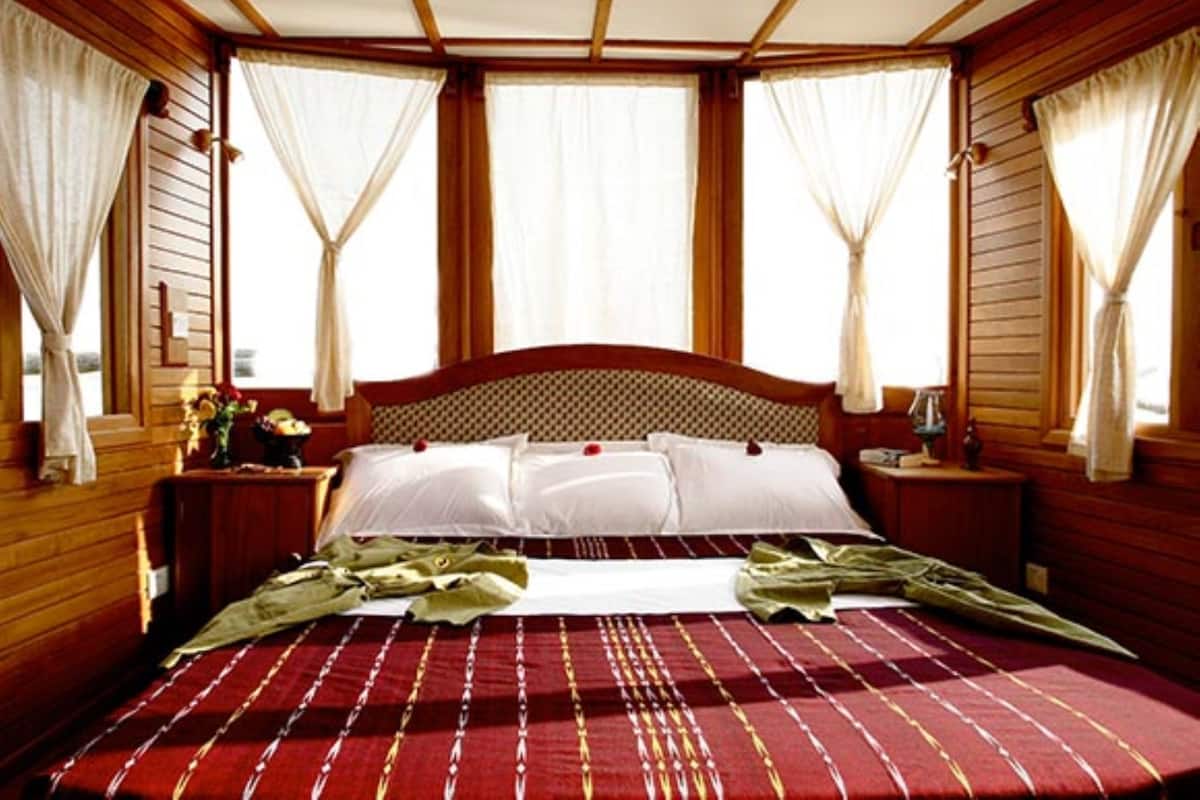 A wooden-paneled bedroom with a large bed, white linens, and curtains.