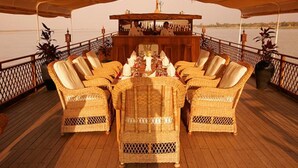 A covered outdoor dining area with wicker furniture and a bar. - Amara River Cruise (Mandalay)