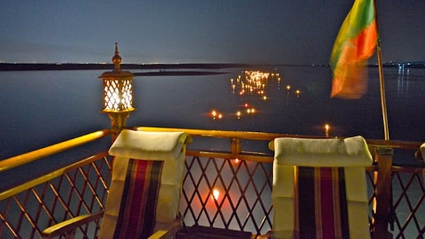 A balcony with a railing, a flag, and a lantern. - Amara River Cruise (Mandalay)