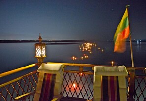 A balcony with a railing, a flag, and a lantern. - Amara River Cruise (Mandalay)