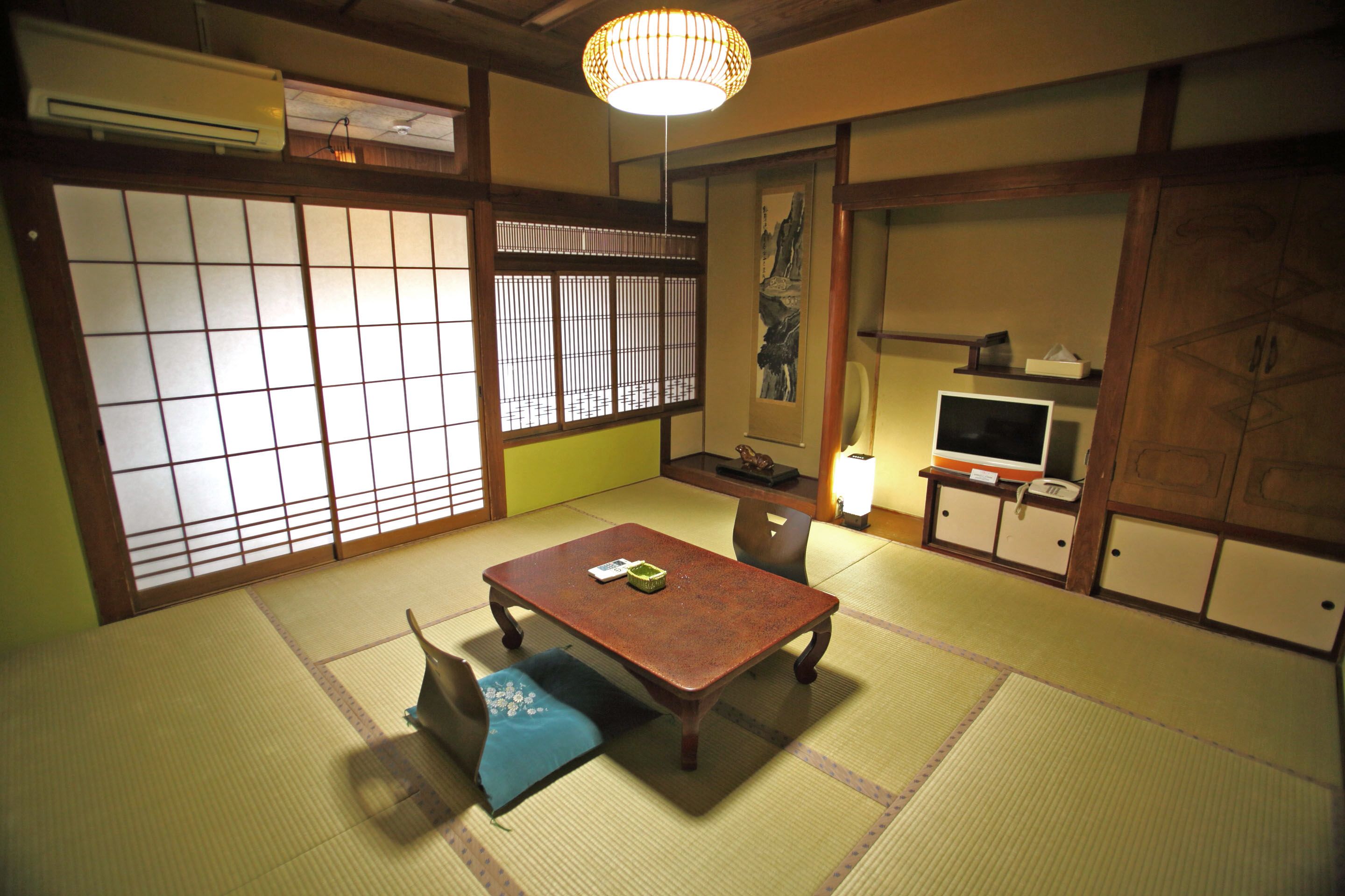 Una habitación japonesa tradicional con suelo de tatami, una mesa baja, un televisor y puertas correderas.