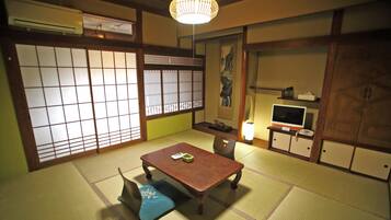Una habitación japonesa tradicional con suelo de tatami, una mesa baja, un televisor y puertas correderas.