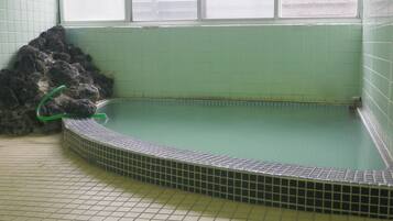 Una piscina pequeña y rectangular con borde de azulejos y un tono verdoso, rodeada de suelo y paredes con baldosas.