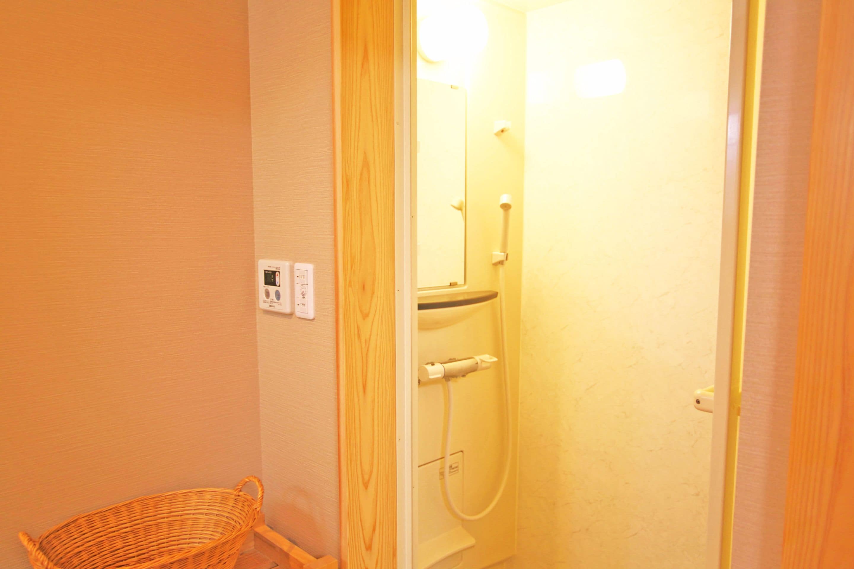 A small bathroom with a shower, a wicker basket, and a wall-mounted electrical outlet.