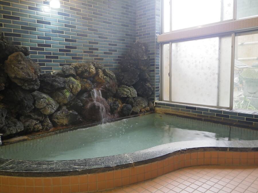 A spa area with a stone wall, a small waterfall, and a tiled floor.