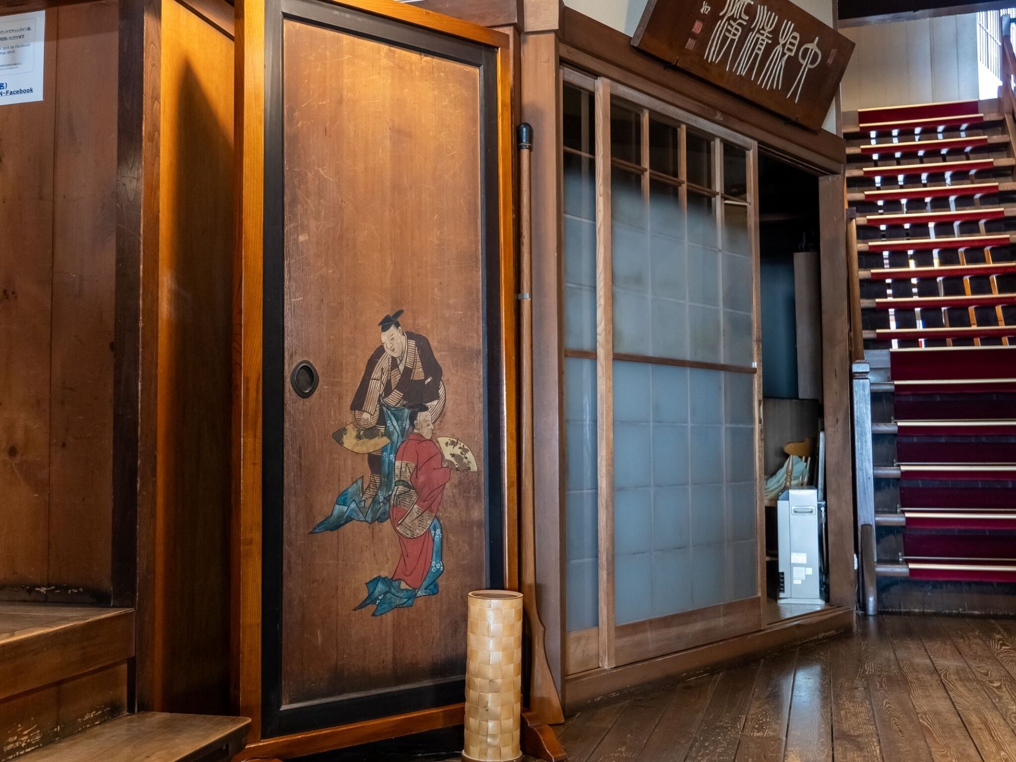 Een traditionele Japanse kamer met tatami vloerbedekking, een shoji schuifdeur en een houten glijdeur met een decoratief schilderij.
