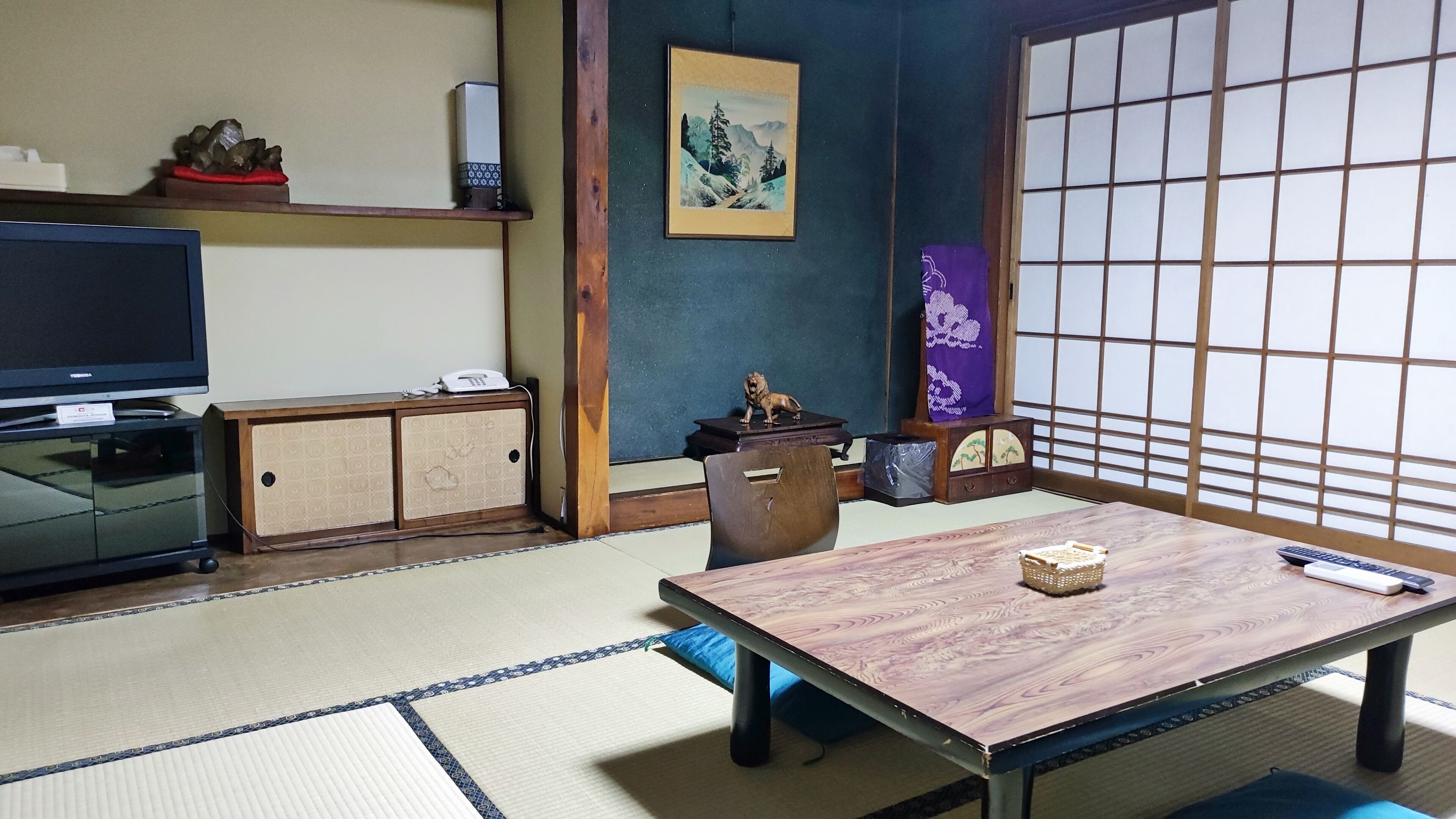 Une pièce de style japonais traditionnel, avec un sol recouvert de tatamis, un téléviseur, une table en bois et un paravent en papier.