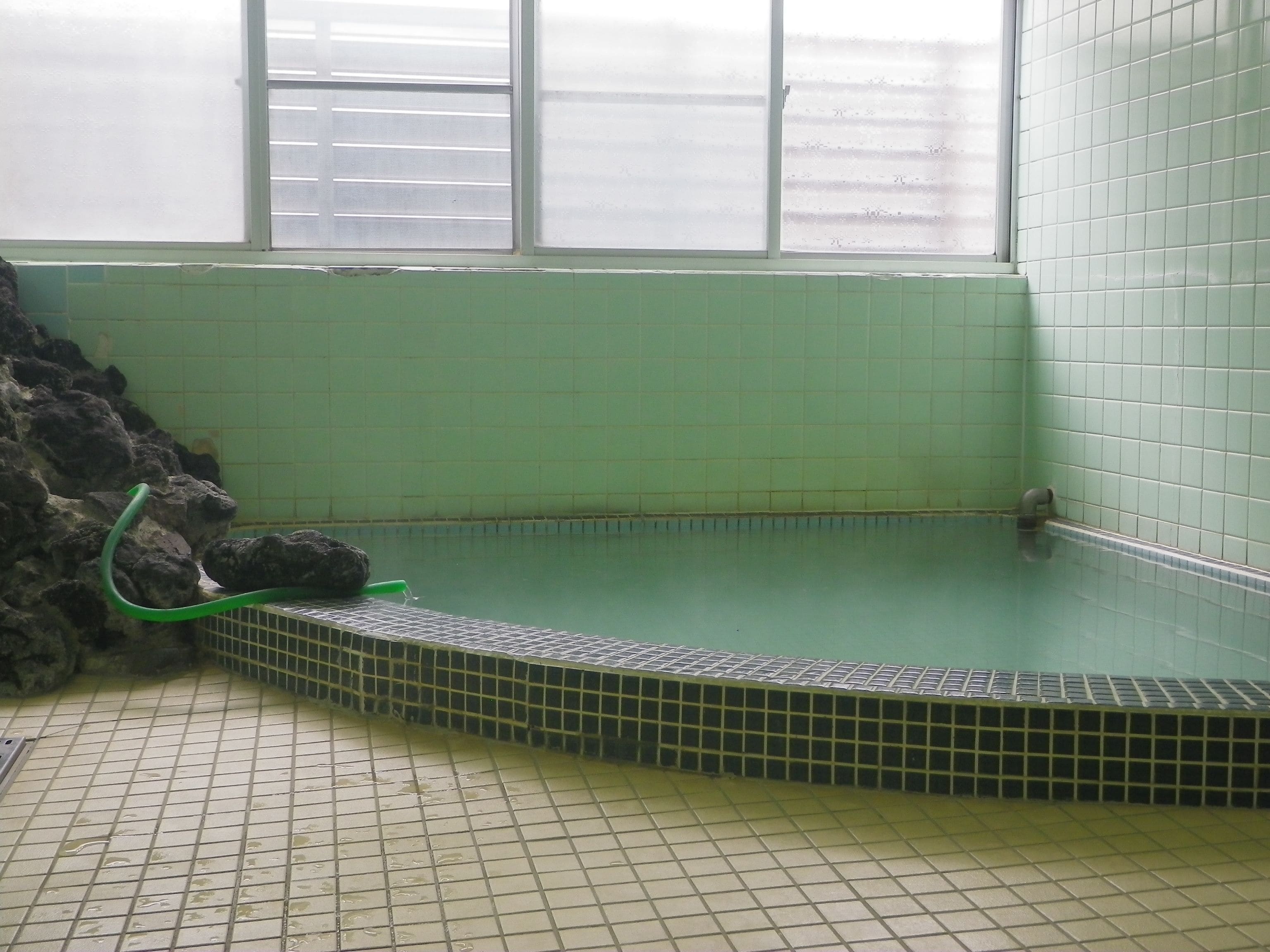 A spa area with a tiled floor, a stone wall, and a window with blinds.