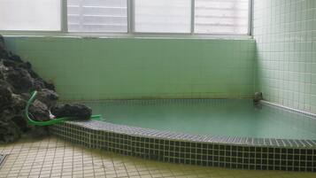 A spa area with a tiled floor, a stone wall, and a window with blinds.
