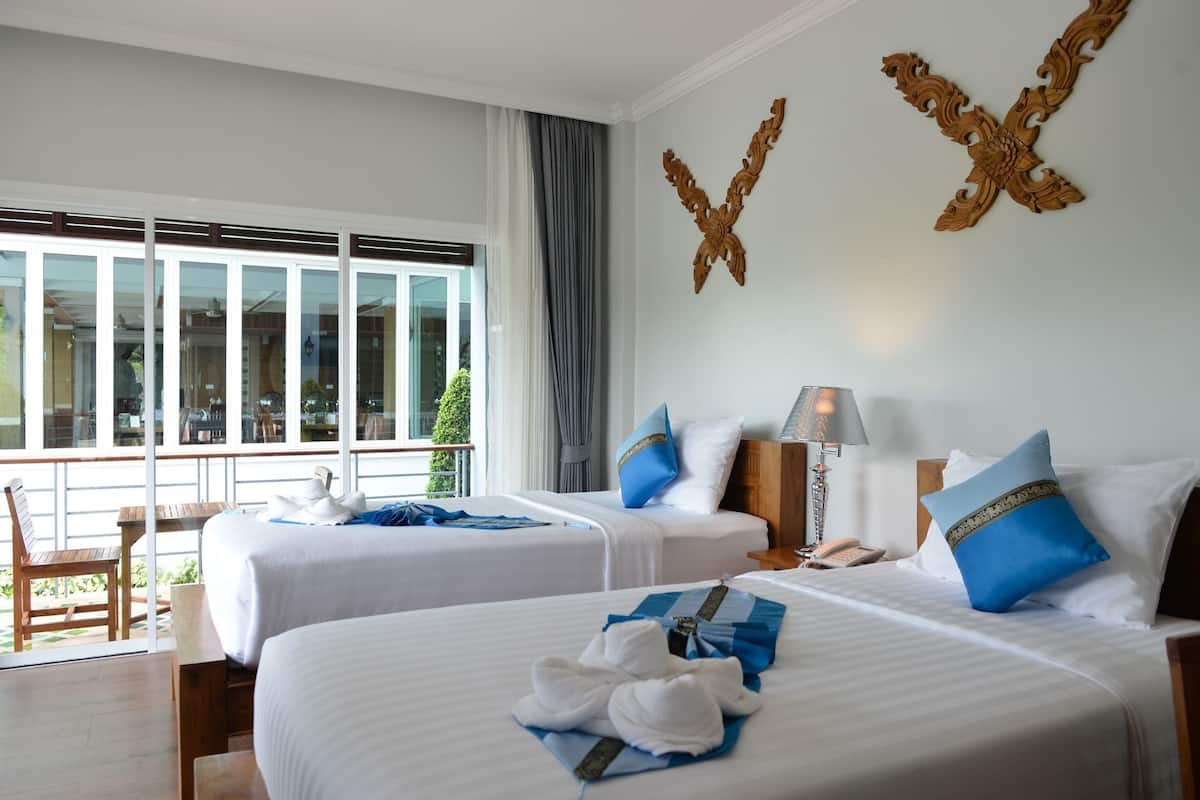 Habitación de hotel con dos camas, balcón, vistas al exterior y un elemento decorativo en la pared.