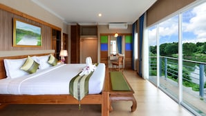 Habitación de hotel con una cama grande, un escritorio, una silla y un balcón con vistas a zonas verdes.