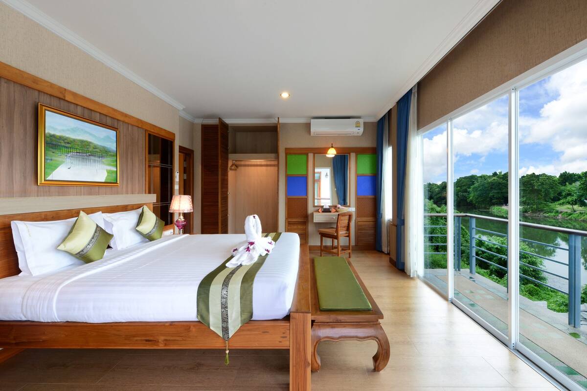 Habitación de hotel con una cama grande, un escritorio, una silla y un balcón con vistas a zonas verdes.