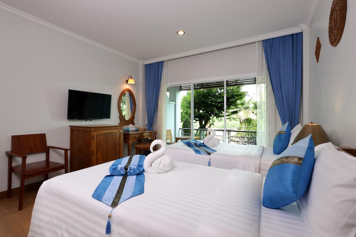 Habitación de hotel con dos camas, televisión, escritorio y vistas a la vegetación.