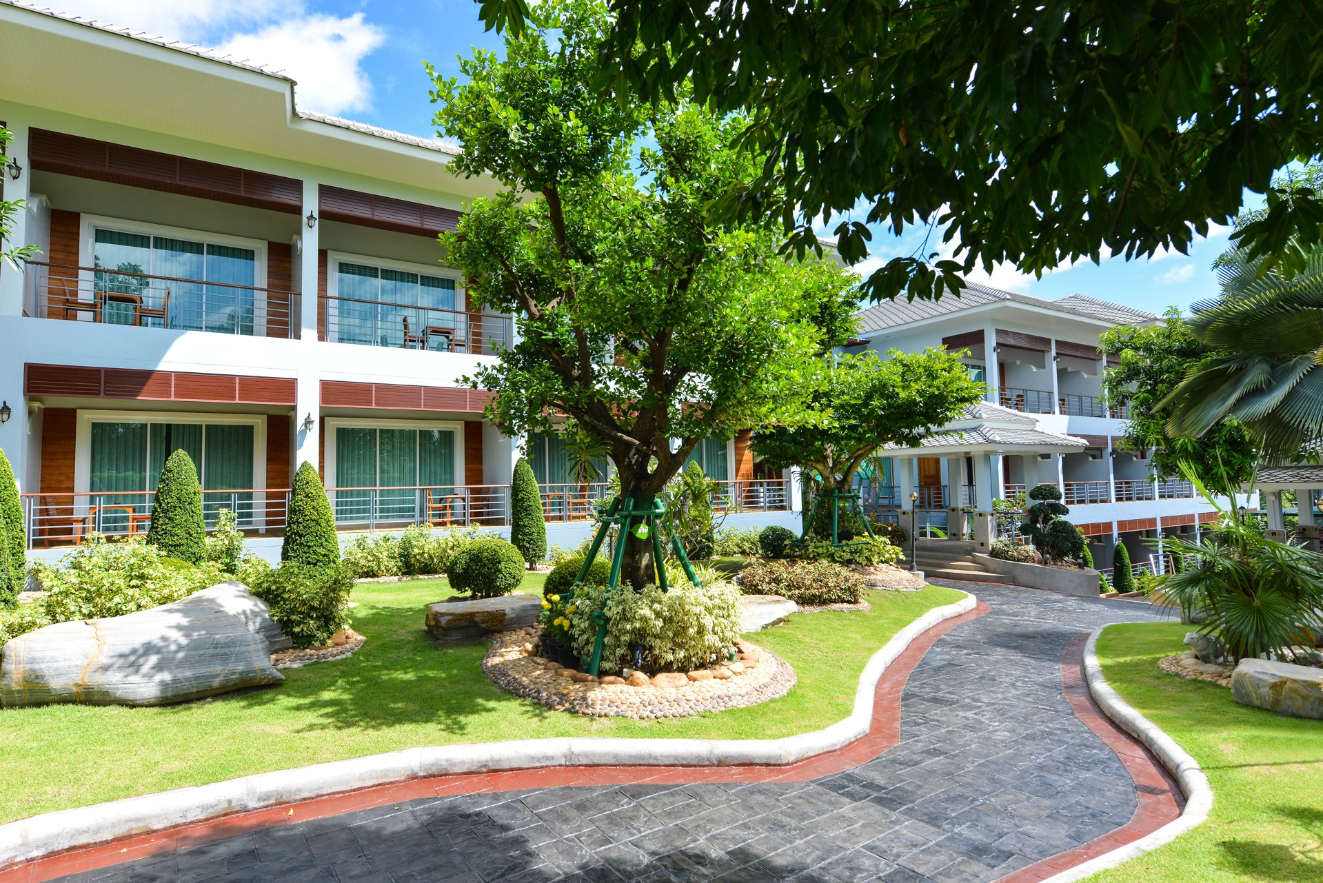 A modern hotel with multiple floors, a central courtyard with a curved pathway, and well-maintained landscaping.