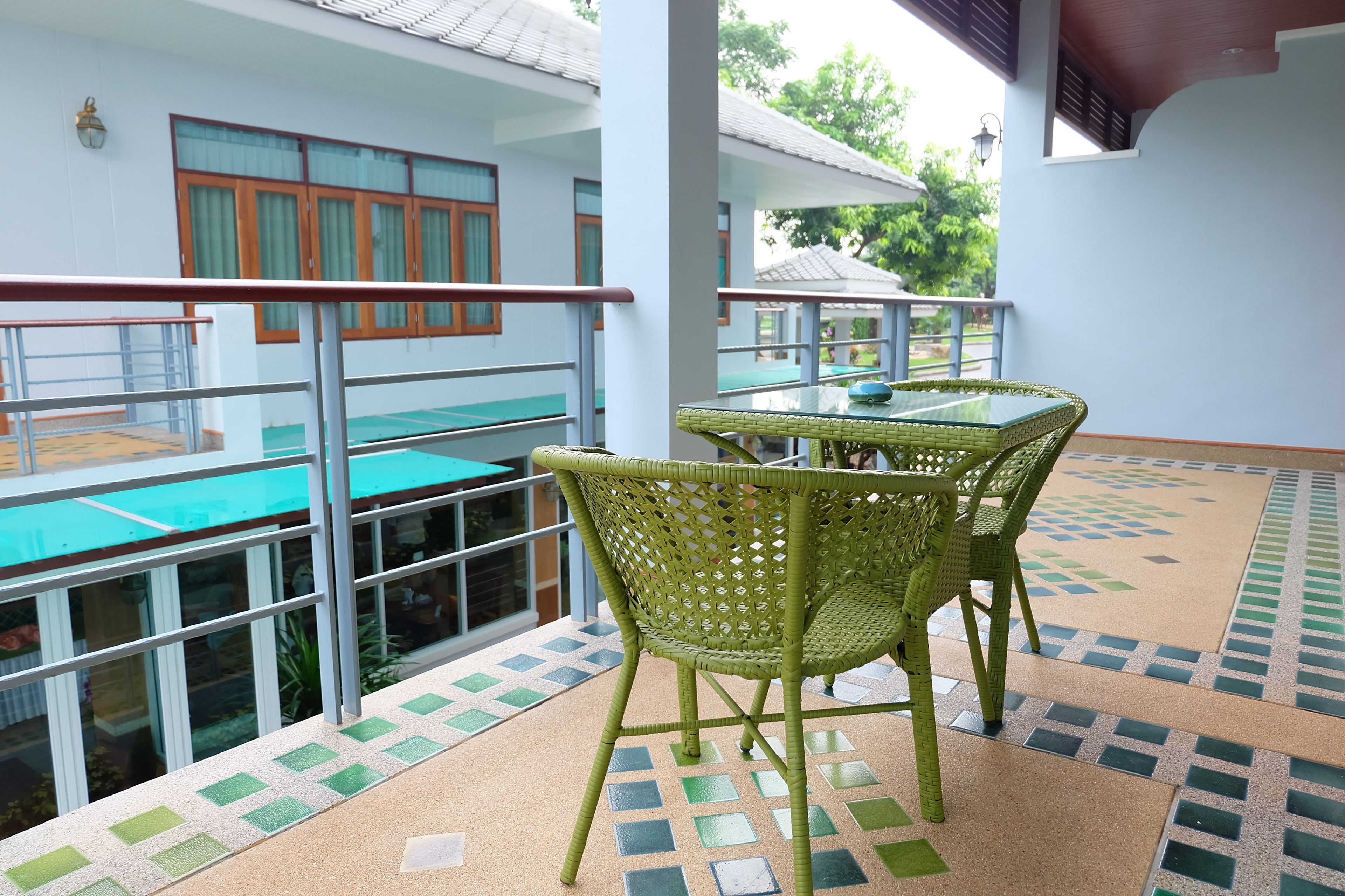 A balcony with a glass railing, a table, and two wicker chairs.