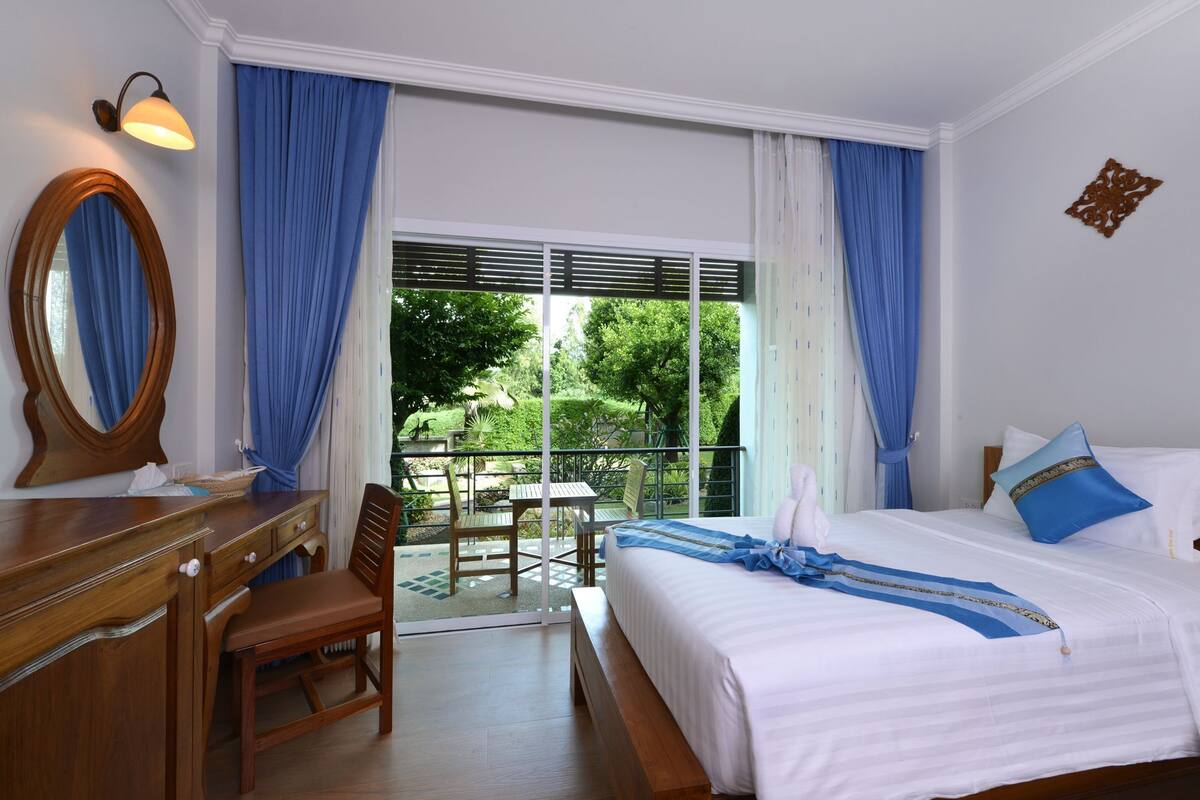 Habitación de hotel con cama, escritorio, silla, cómoda y una ventana grande con cortinas.