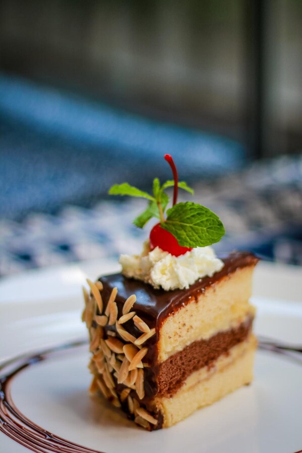 A slice of layered cake with a cherry on top, placed on a plate. - Little PP Hometel (Surat Thani)