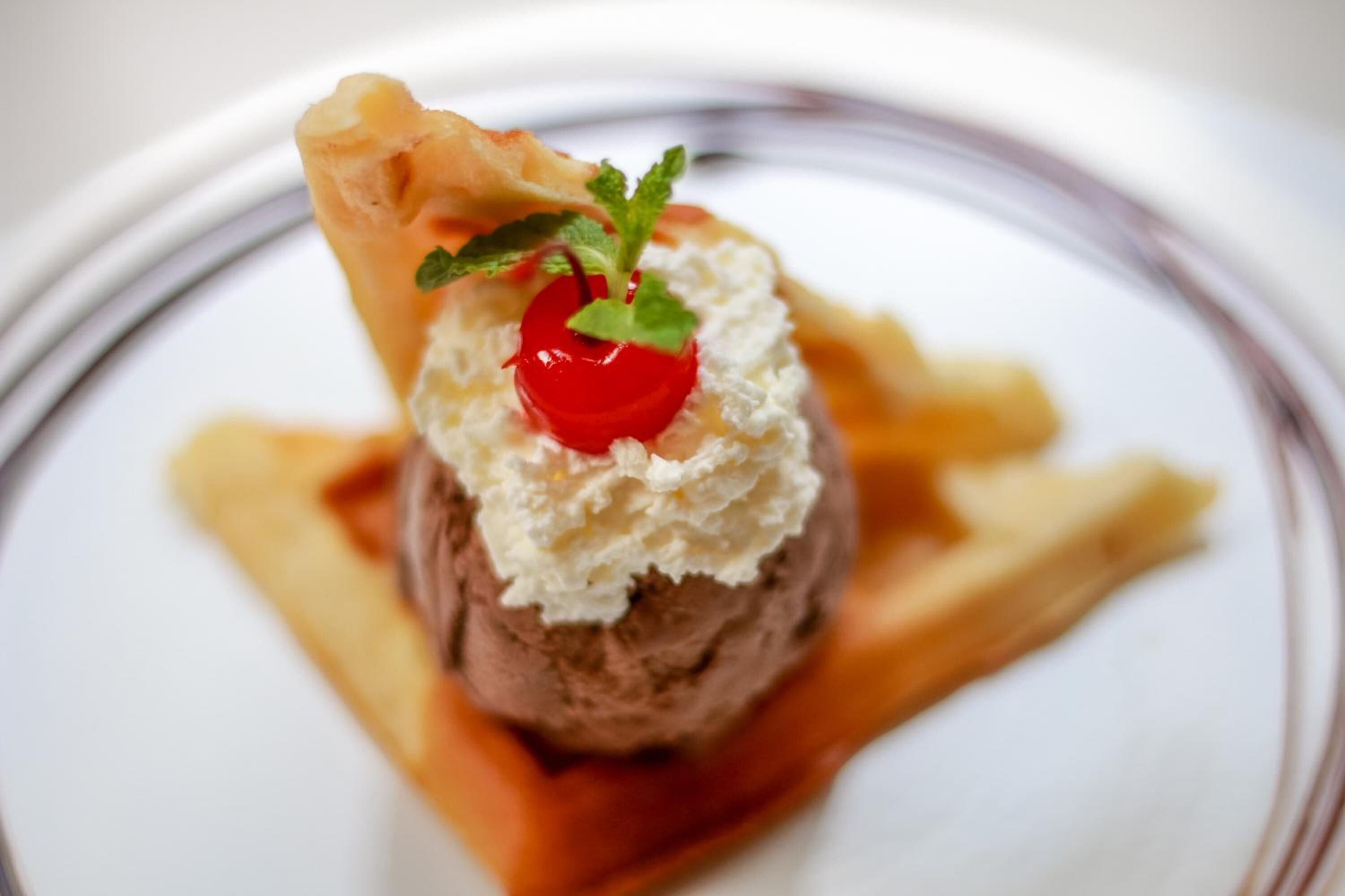 A dessert with a cherry on top, served on a plate with a sauce and a piece of pastry.
