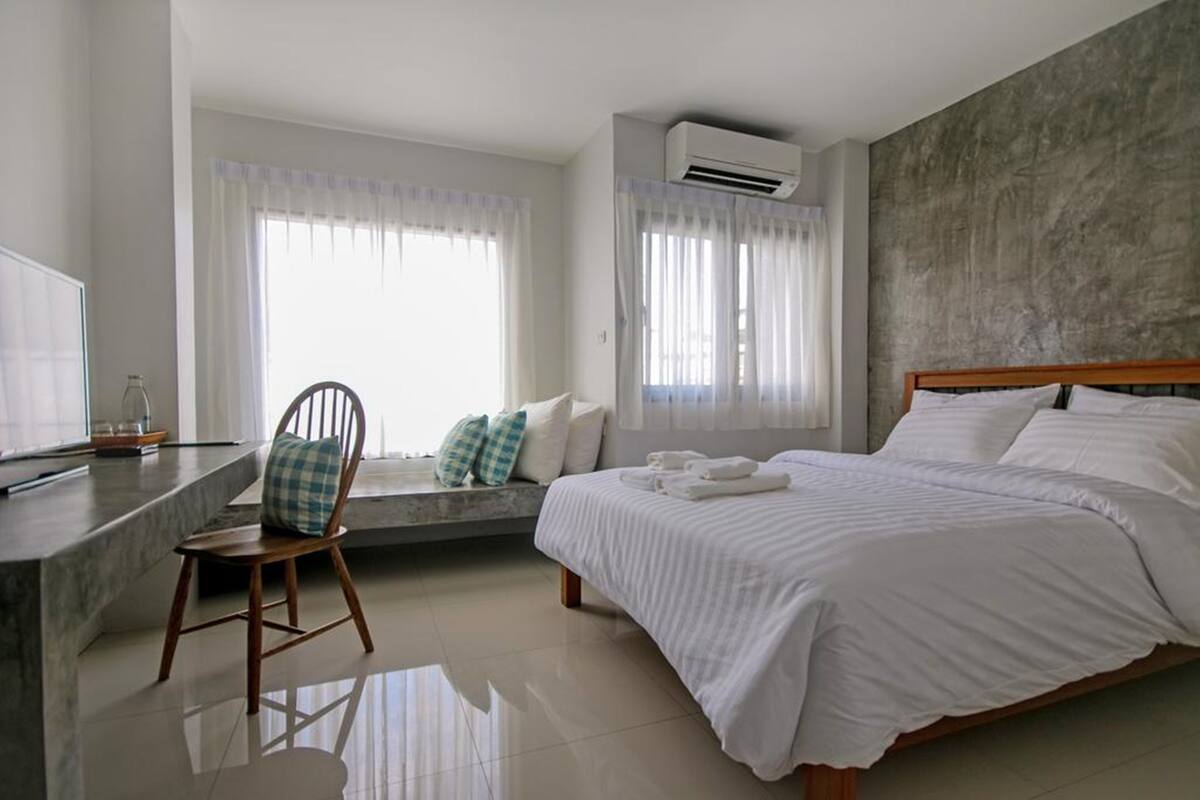 Un dormitorio con una cama, una silla, un escritorio y un ventanal con cortinas.