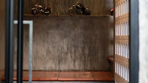 A narrow hallway with a concrete wall, two motorcycles on a shelf, and a wooden partition with a grid pattern. - Little PP Hometel (Surat Thani)
