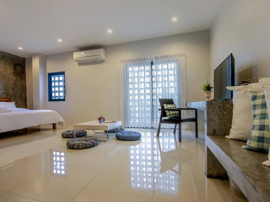 A modern hotel room with a bed, a sofa, a TV, and a window with curtains.