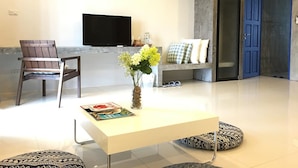 A modern living room with a flat-screen TV, a coffee table, a chair, and a bench with cushions. - Little PP Hometel (Surat Thani)