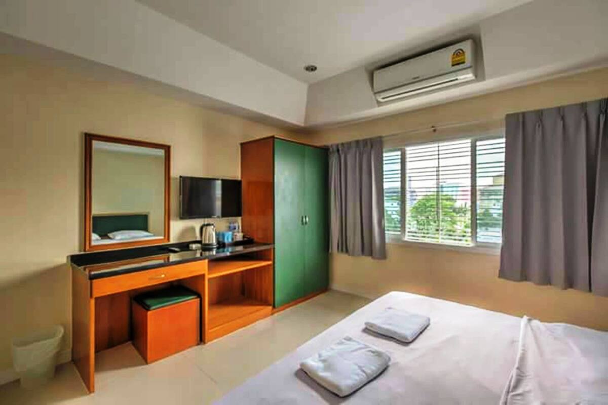 A hotel room with a bed, a desk with a chair, a wardrobe, a television, and a window with curtains.