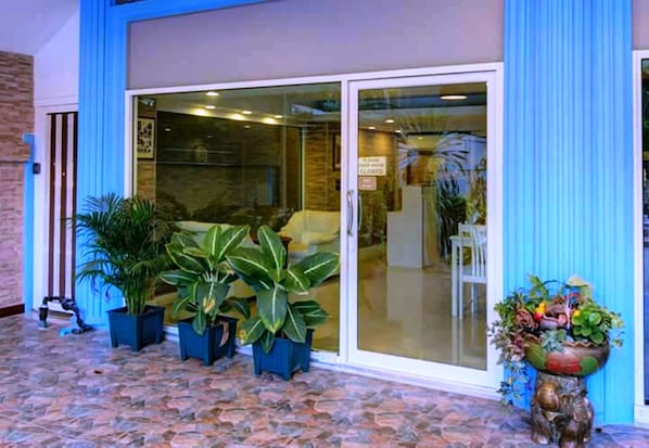 Hotel entrance features a large glass door and stone-tiled patio area surrounded by potted plants.
