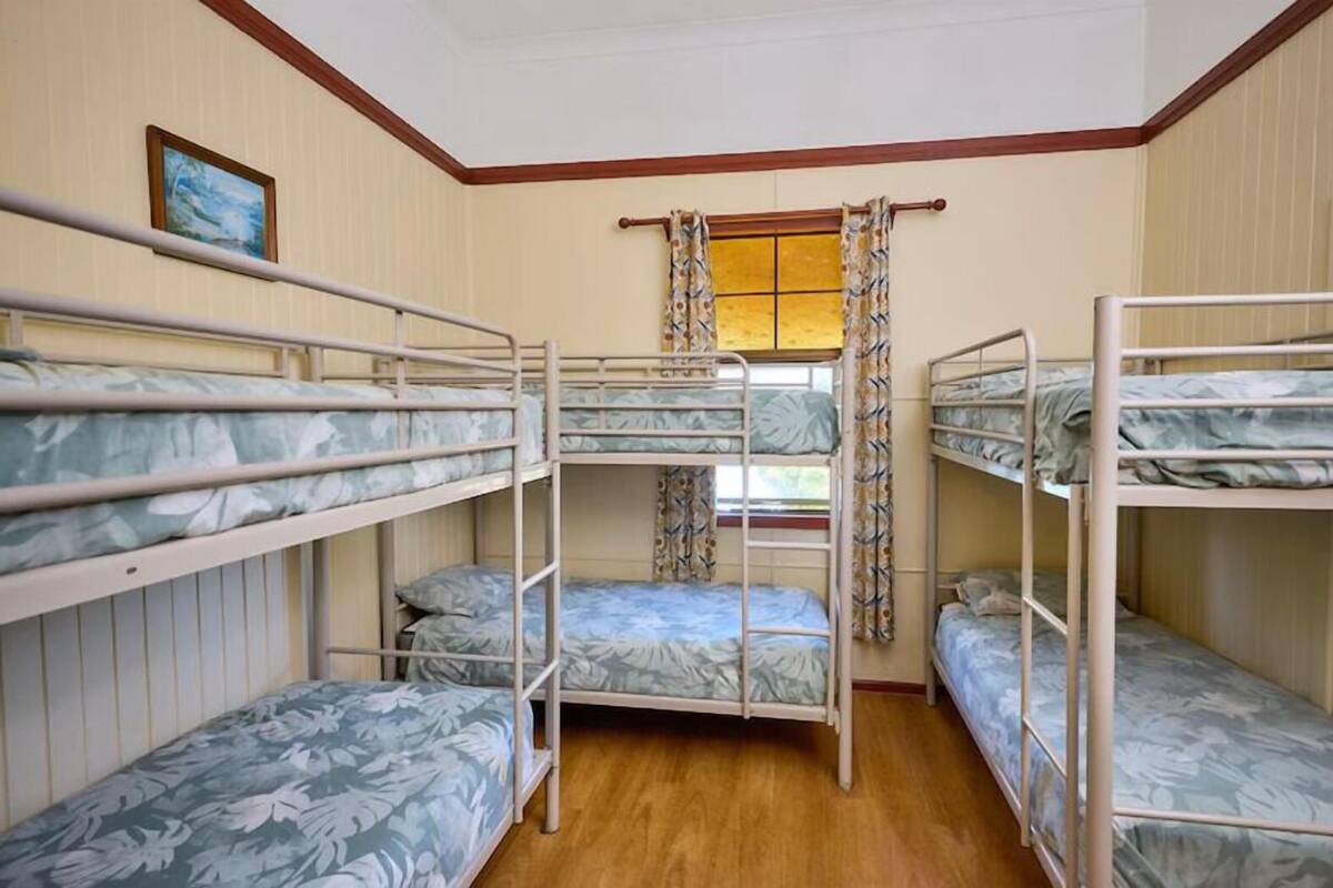 Una habitación con literas, suelo de madera, una ventana con cortinas e imagen enmarcada en la pared.