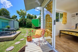 Un patio con una mesa y sillas, un pequeño jardín con piedras para el camino, y una casa móvil verde al fondo.