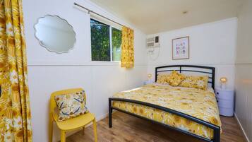 Un dormitorio con cama, una silla, un ventanal y un espejo instalado en la pared.
