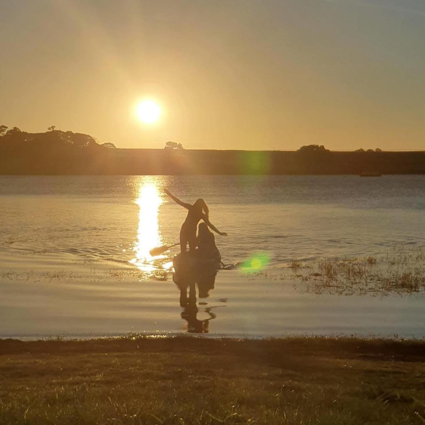 A sunset over a calm body of water with a silhouette of a person and a dog.