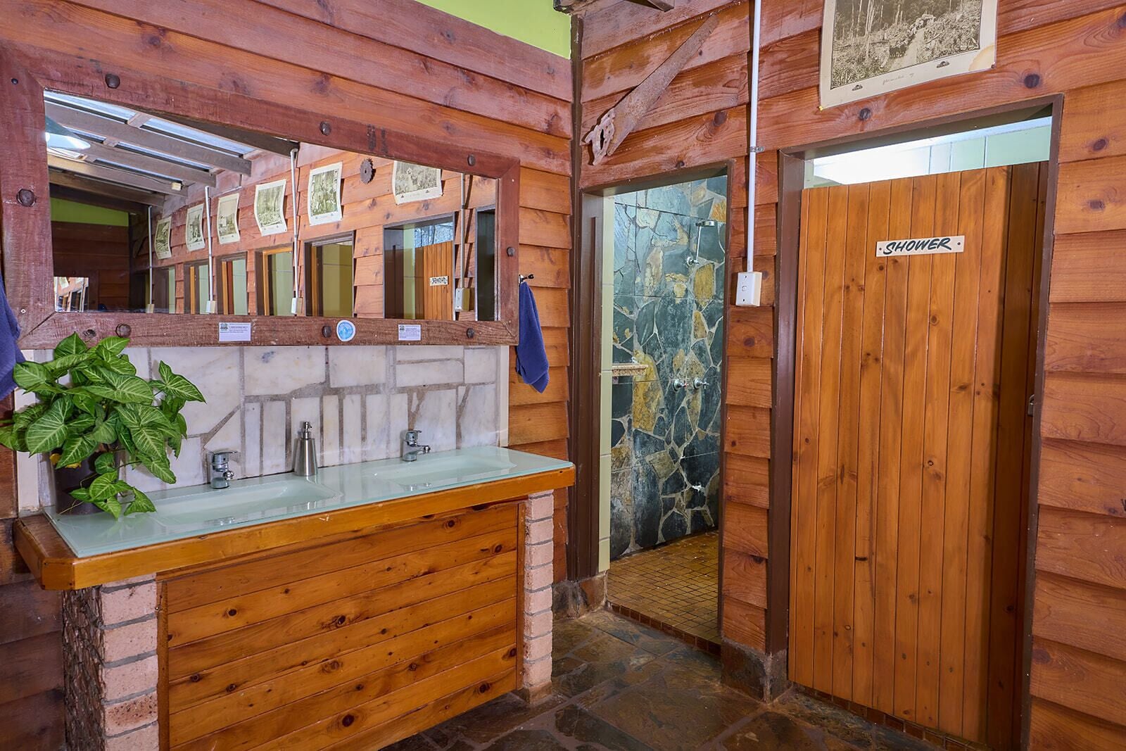 Une salle de bain rustique, avec des murs en bois, un mur de douche en pierre, un lavabo en bois et un miroir.
