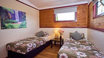 Un dormitorio con dos camas individuales, una mesita de noche con lámpara, un cuadro de una cascada y una ventana con marco de madera.