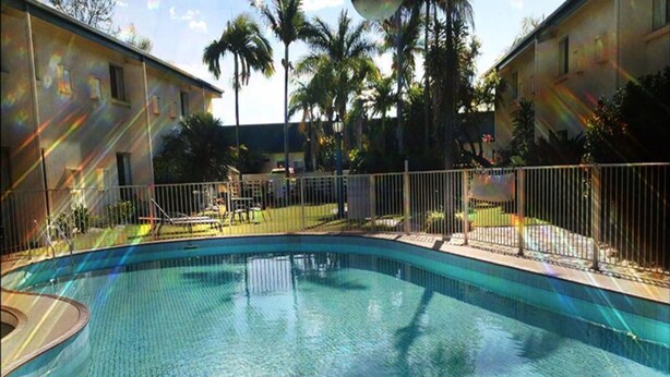 A swimming pool with a metal ladder, surrounded by a fence and palm trees. - Emerald Central Hotel (Emerald)
