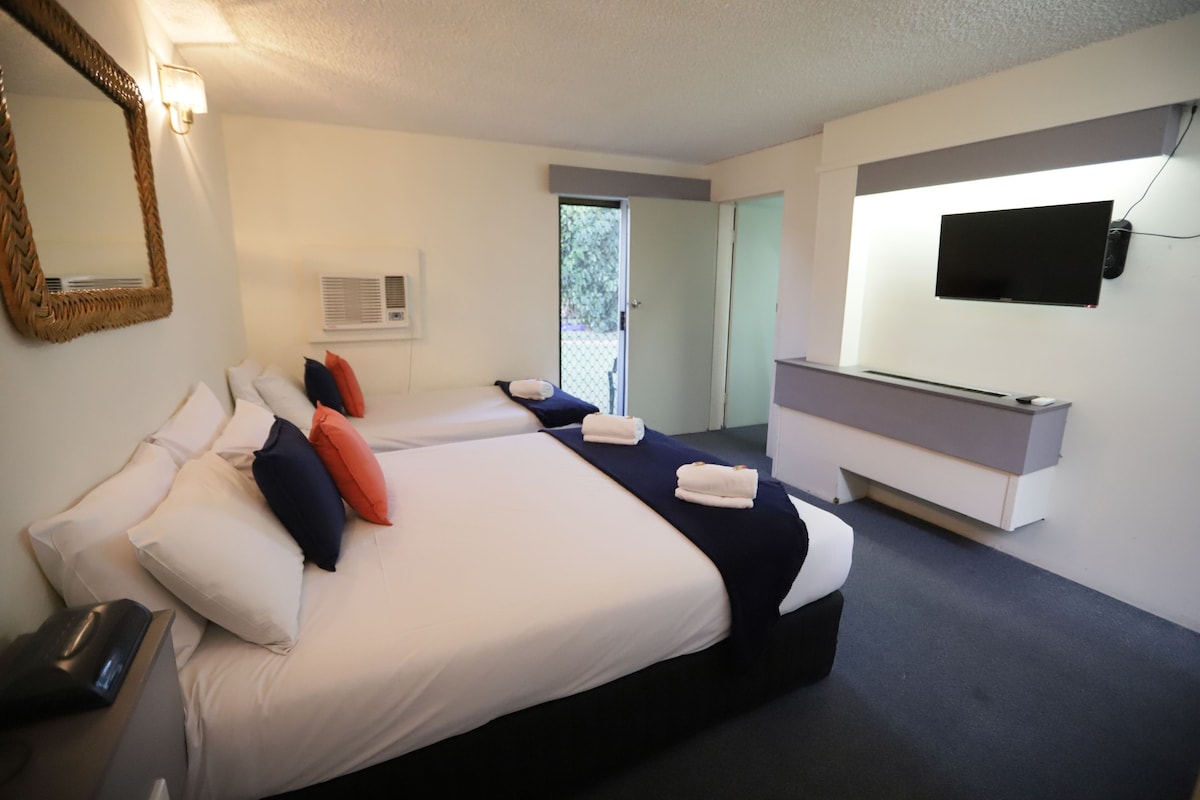 Une chambre d’hôtel avec deux lits, une télévision, un miroir et une porte donnant sur l’extérieur.