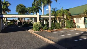 A gas station with a clear height sign, palm trees, and a building with a green roof. - Emerald Central Hotel (Emerald)