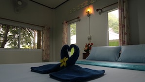 A hotel room with a bed, two windows with curtains, a bedside table with a vase of flowers, and a wall-mounted light fixture. - Koh Phayam Greentawan Resort (Ranong)