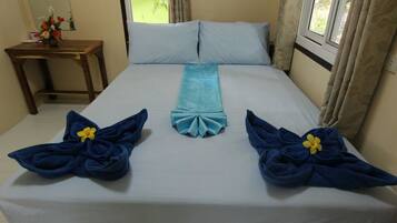 Una cama bien hecha con una colcha azul claro, dos toallas azules con flores amarillas y una mesita de noche de madera con un florero.
