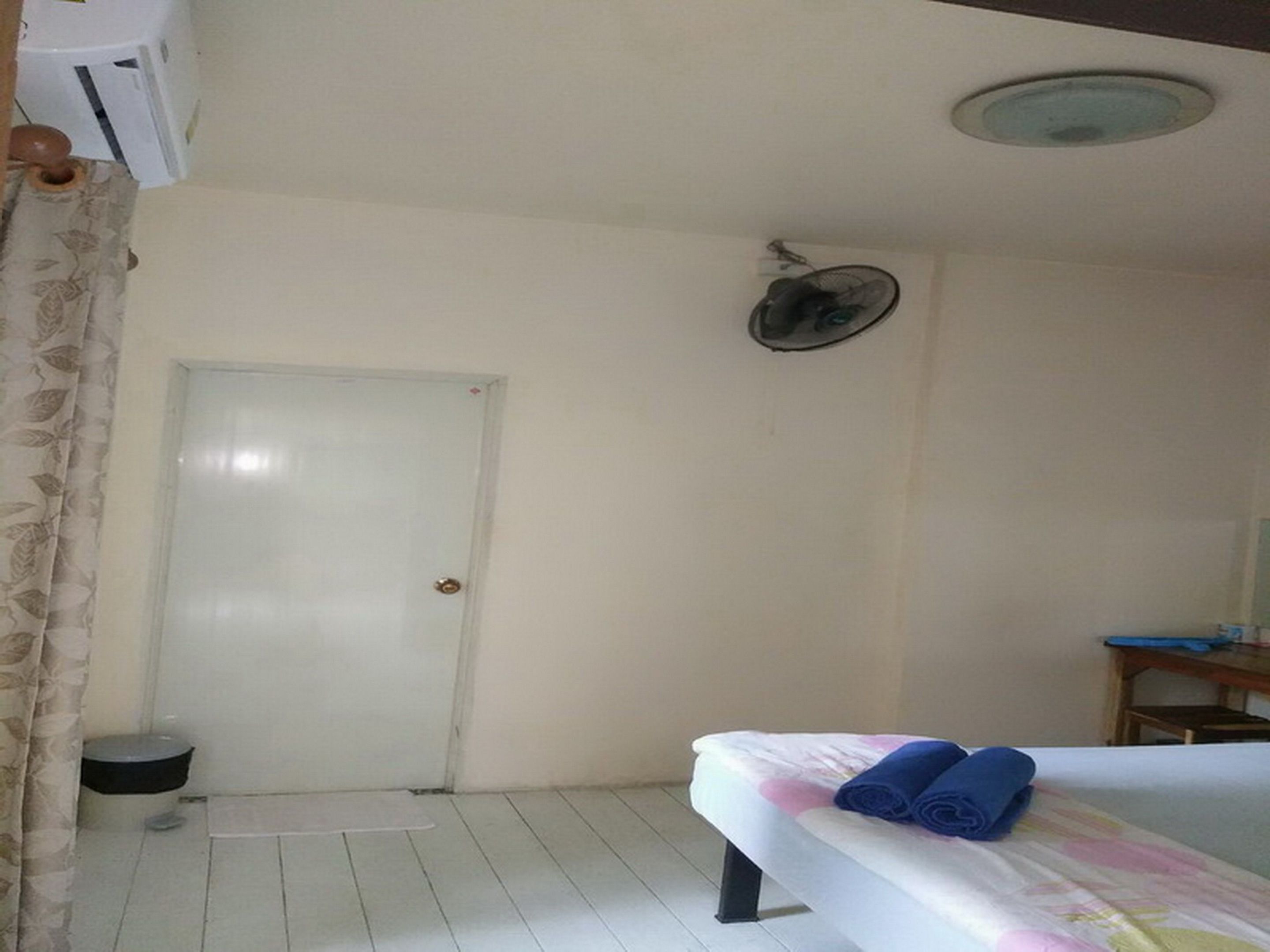 Una habitación de hotel con una cama, un ventilador de techo, una puerta y una pequeña mesa con una silla.