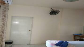 Una habitación de hotel con una cama, un ventilador de techo, una puerta y una pequeña mesa con una silla.