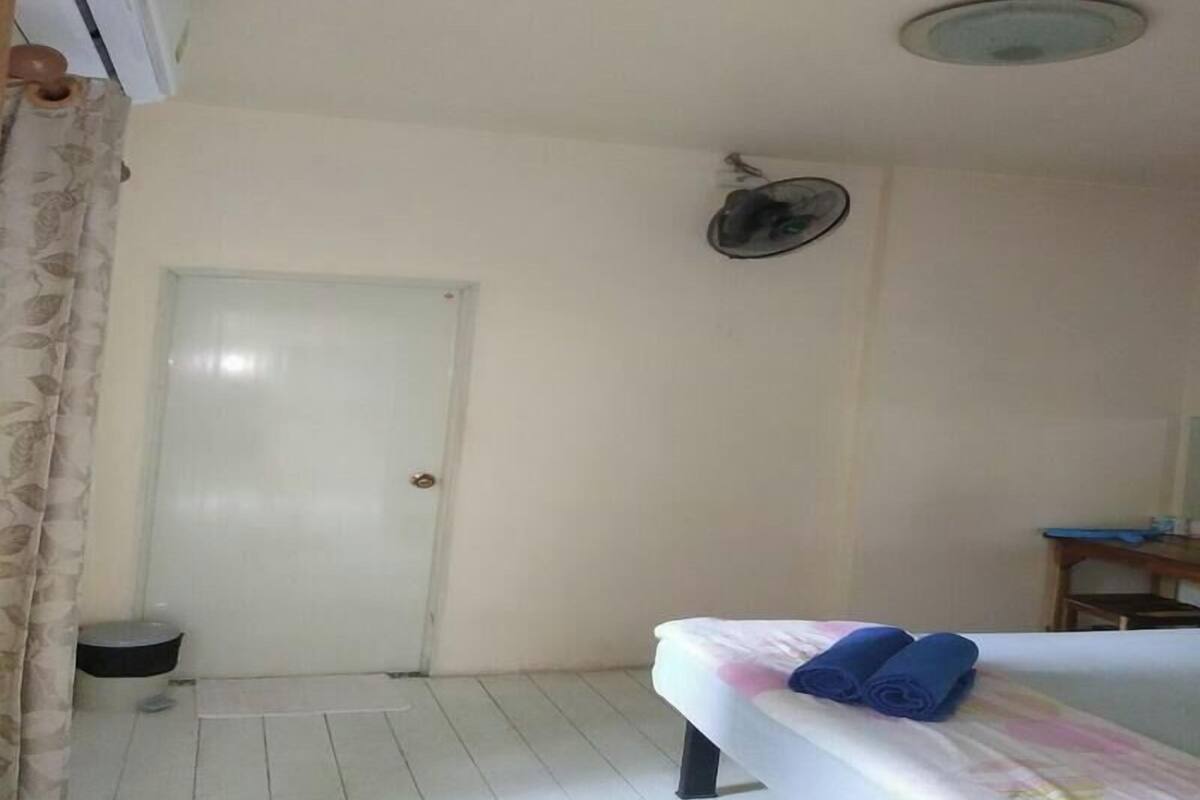 Una habitación con una cama, una puerta, un ventilador y una mesita.