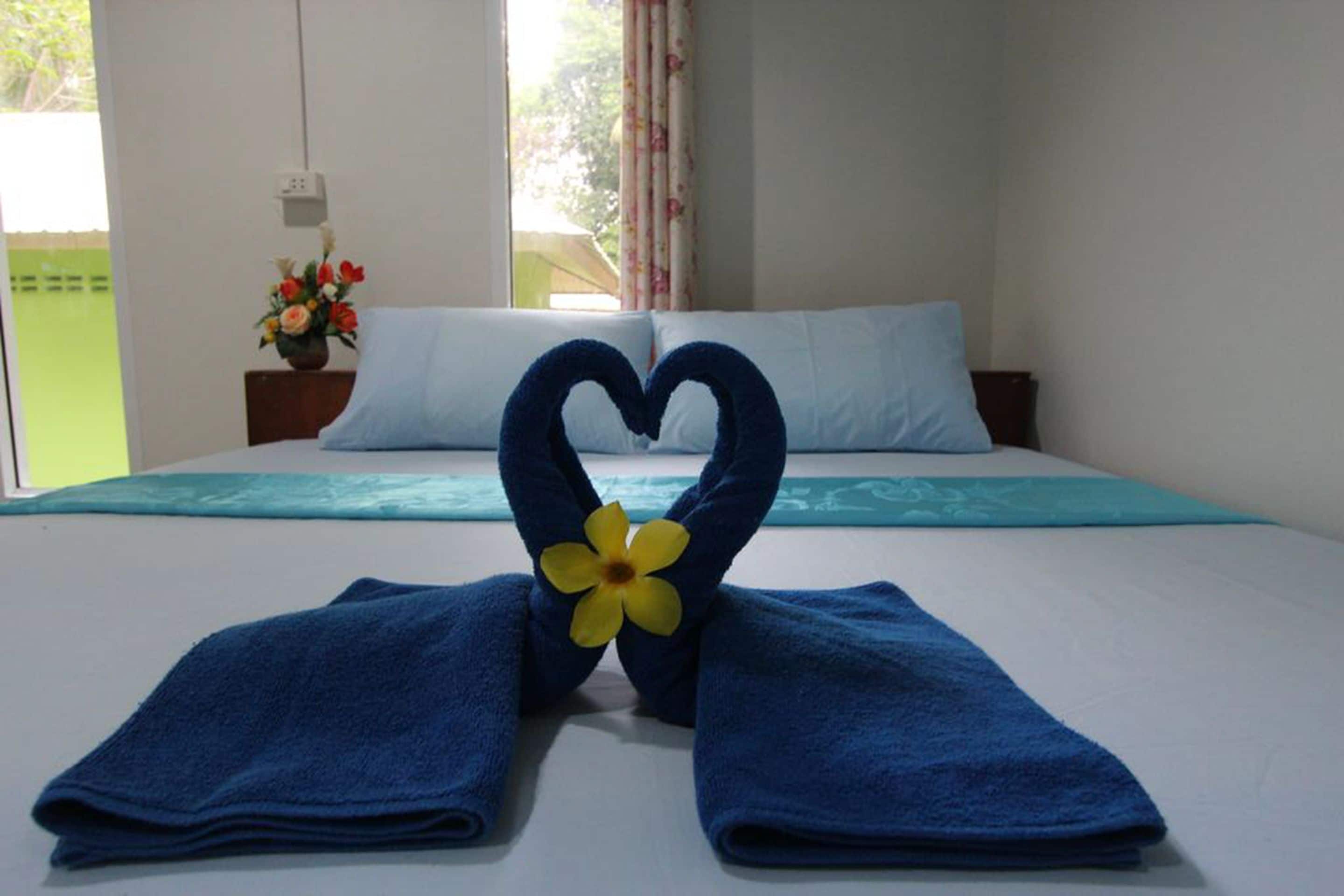 Una habitación de hotel con una cama, una toalla dispuesta en forma de corazón y una decoración floral.