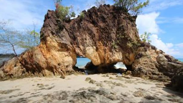 A natural rock formation with a cave-like opening, surrounded by sandy beach and sparse vegetation. - Koh Phayam Greentawan Resort (Ranong)