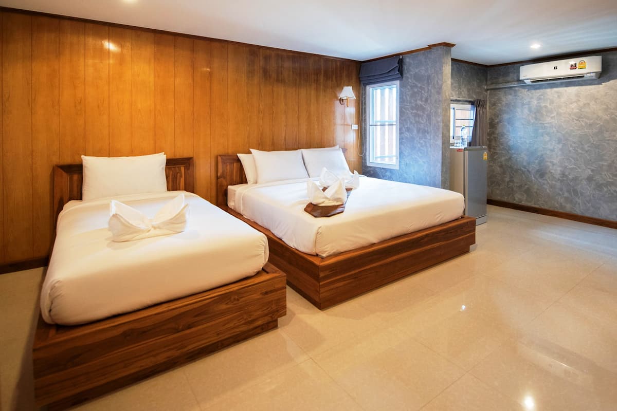 Quarto de hotel com duas camas de madeira, uma janela com cortinas, um ar condicionado e um frigorífico.