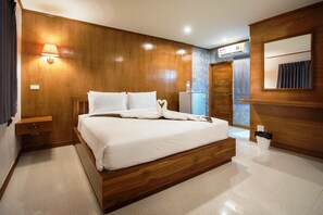 A modern hotel room with a wooden bed, a nightstand, a wall-mounted lamp, a mirror, and a built-in air conditioning unit. - Viking Resort (Pattaya)